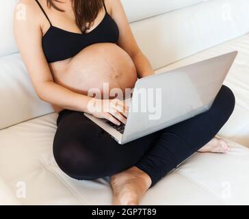 Schwangere Frau mit Bauch mit einem Laptop auf dem Sofa Stockfoto