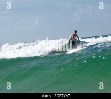 Surfer auf Longboard reitet eine schöne blaue Welle im Meer. Stockfoto