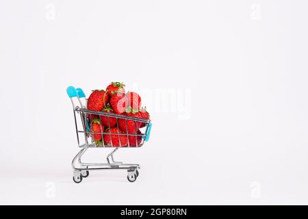Spielzeug-Einkaufswagen oder -Trolley voll von reifen großen roten Erdbeeren isoliert auf weißem Hintergrund. Berry Ernte Verkaufskonzept. Banner mit Kopierbereich Stockfoto