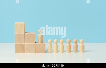 Holzfiguren von Männern auf einer Leiter aus Blöcken. Das Konzept der beruflichen Weiterentwicklung, Start bei der Arbeit, Ziele zu erreichen. Blauer Hintergrund Stockfoto