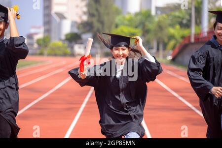 Glückliche Abschlussstudenten mit Diplom und laufen auf dem Stadion In der Schule Stockfoto