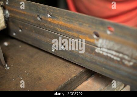 Gebohrte Löcher in das Metall. Arbeiten Sie in einer Metallwerkstatt. Die Hand hält einen Stahlrohling. Ein Mann arbeitet in der Garage. Stockfoto