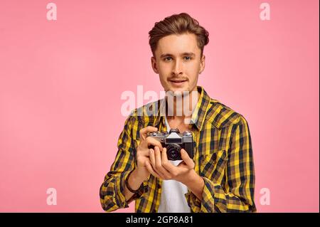 Porträt eines jungen Fotografen mit einer Kamera, rosa Hintergrund. Gesichtsausdruck, männliche Person posiert im Studio, Genrekonzept, Beruf Stockfoto