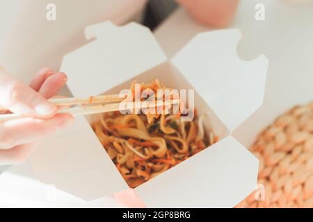 Wok-Nudeln in der Take-away-Box. Frau beim Essen mit Essstäbchen, Nahaufnahme auf weiblichen Händen. Traditionelle chinesische Küche mit Gemüse und Meeresfrüchten. Stockfoto