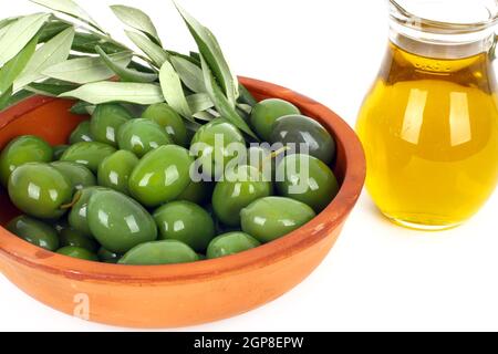 Olivenöl aus einem Krug in einer Terrakotta-Schale mit den Zweigen eines Olivenbaums fließen Stockfoto