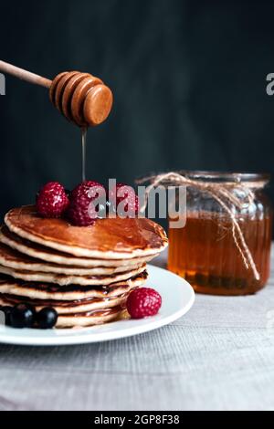 Saftige Pfannkuchen mit Beeren und Honig auf einem weißen Teller, Löffel, Glas, Holztisch. Hochwertige Fotos Stockfoto