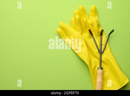 Gelbe Gummihandschuhe und Metall Garten kleine Rechen auf grünem Hintergrund, kopieren Raum Stockfoto