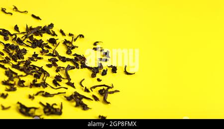 Trockene schwarze lose Teeblätter auf gelbem Brett, Nahaufnahme Detail von oben, Platz für Text rechts. Stockfoto