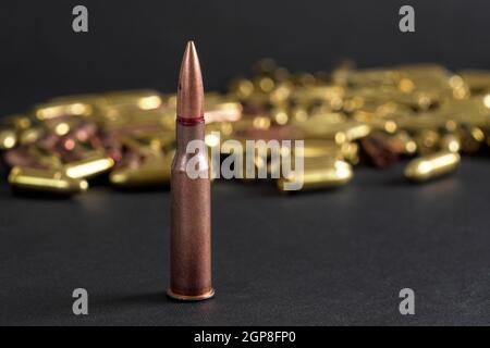 Kupferne Maschinengewehr Kugel, verschwommene gelbe Ammo auf schwarzem Brett Hintergrund. Stockfoto