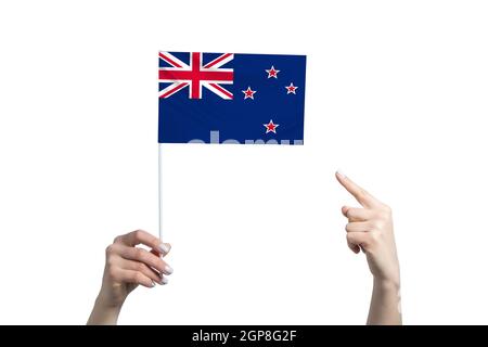 Eine schöne weibliche Hand hält eine neuseeländische Flagge, zu der sie den Finger ihrer anderen Hand zeigt, isoliert auf weißem Hintergrund. Stockfoto