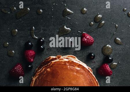 Saftige Pfannkuchen mit Beeren, Honig, Löffel auf einem schwarzen und grauen Betontisch. Hochwertige Fotos Stockfoto
