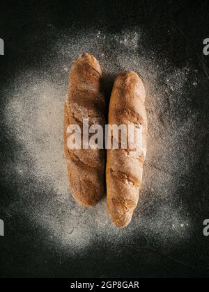 Zwei ganze hausgemachtes Brot Brot mit Buchweizen Buchweizen Mehl auf Schwarz strukturierten Hintergrund. Ansicht von oben oder flach-legen. Low Key Stockfoto