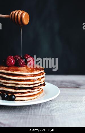 Saftige Pfannkuchen mit Beeren und Honig auf einem weißen Teller, Löffel, Holztisch. Hochwertige Fotos Stockfoto