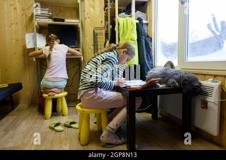 Zwei Mädchen machen Hausaufgaben am Computertisch und Der Tisch, auf dem die Katze am Fenster schläft In einem kleinen Raum eines Landhauses Stockfoto