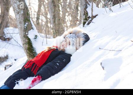 Das Mädchen fiel in eine Schneewehe mit ihrem Rücken und Schaute in den Rahmen in einem verschneiten Wald Stockfoto