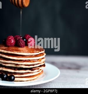 Saftige Pfannkuchen mit Beeren und Honig auf einem weißen Teller, Löffel, Holztisch. Hochwertige Fotos Stockfoto