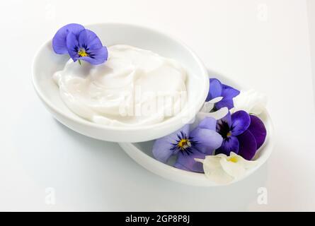 Salbe aus Viola oder violetten Blüten in weißen Schalen, Naturkosmetik-Konzept, weißgrauer Hintergrund, Kopierraum, ausgewählter Fokus, Geringe Tiefe der Fi Stockfoto