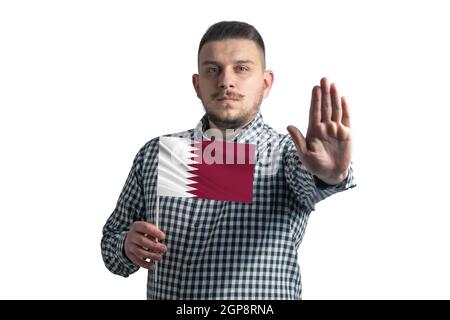 Weißer Kerl hält eine Flagge von Katar und mit einem ernsten Gesicht zeigt eine Hand Stop-Zeichen isoliert auf einem weißen Hintergrund. Stockfoto