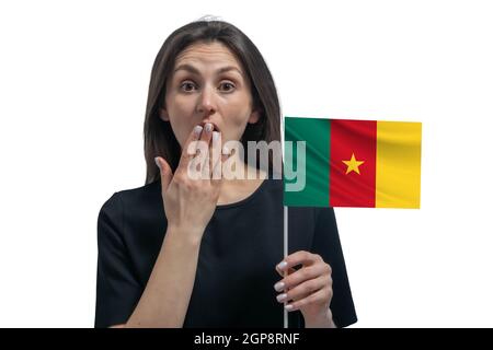 Glückliche junge weiße Frau hält Flagge von Kamerun und bedeckt ihren Mund mit ihrer Hand isoliert auf einem weißen Hintergrund. Stockfoto