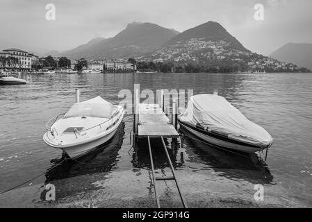 Berge und See in Lugano in der Schweiz. Die Boote sind im Vordergrund. Die Schwarz-Weiß-Fotografie. Stockfoto