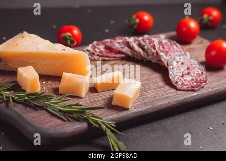 Geräucherte Schinkenwurst und geschnittene Scheiben mit Rosmarin und Kirsche Tomaten auf dunklem Holzbrett Stockfoto