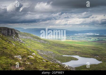 Grüne Felder und große Felsbrocken im Cuilcagh Mountain Park mit kleinen Seen im Tal unten, Nordirland Stockfoto