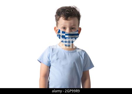 Atemschutzmaske mit Flagge von Griechenland. Weißer Junge setzt auf medizinische Gesichtsmaske isoliert auf weißem Hintergrund. Stockfoto