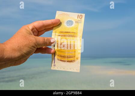 Eine Touristenschau der maledivischen Rufiyaa Banknote, wenn sie auf den Malediven unterwegs ist. Geldschein der Malediven in weiblicher Hand auf dem Hintergrund des Ind Stockfoto