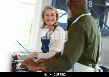 Glückliches, vielseitiges Paar in der Küche, das Schürzen trägt und zusammen kocht Stockfoto