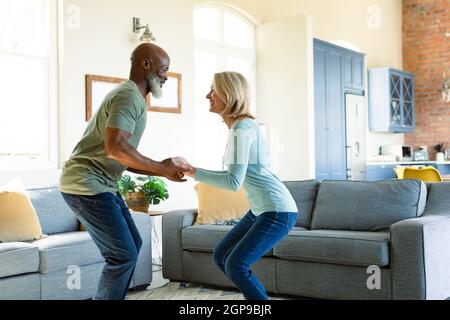 Glückliches, vielseitiges Paar im Wohnzimmer, das zusammen tanzt Stockfoto