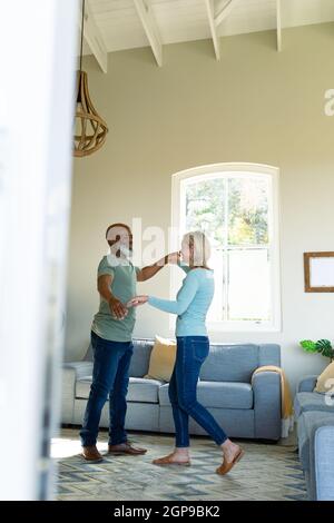 Glückliches, vielseitiges Paar im Wohnzimmer, das zusammen tanzt Stockfoto
