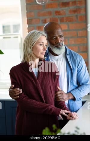 Besorgt Senior diverse Paar in der Küche lehnte sich auf Arbeitsplatte, umarmt und wegschaut Stockfoto