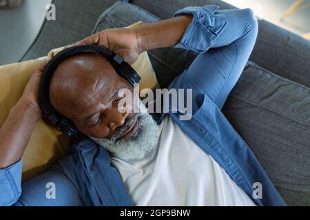 Entspannender afroamerikanischer Mann im Wohnzimmer, der auf dem Sofa lag und Kopfhörer trug Stockfoto