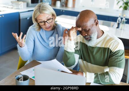 Gestresste ältere verschiedene Paar in der Küche sitzen am Tisch, mit Laptop Stockfoto