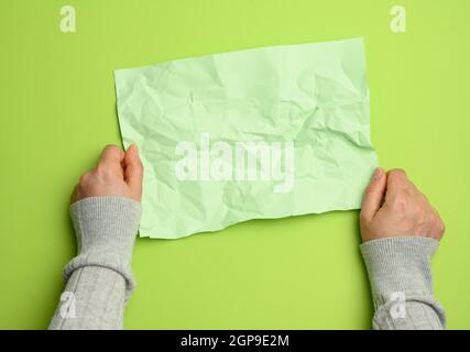 Zwei weibliche Hände halten leere zerknitterte grüne Blatt Papier auf einem grünen Hintergrund, Copy Space, Draufsicht Stockfoto