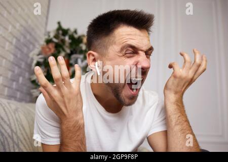 Wütend schreienden jungen Mann in Ohrhörern spricht mit jemandem auf Videoanruf. Stockfoto