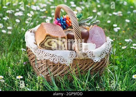 Ostern traditionelle Küche mit Schinken, Eiern und Brot im Korb. Urlaub im Freien. Osterkorb mit allerlei köstlichen Delikatessen gefüllt Stockfoto