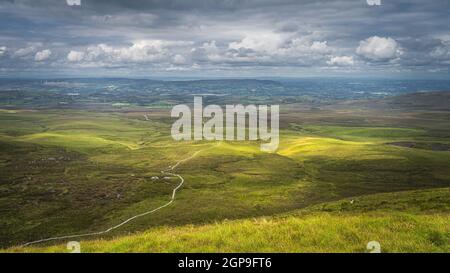 Gewundene Holzweg der Cuilcagh Mountain Park Promenade, beleuchtet von Flecken von Sonnenlicht im Tal unten mit dramatischen Himmel, Nordirland Stockfoto