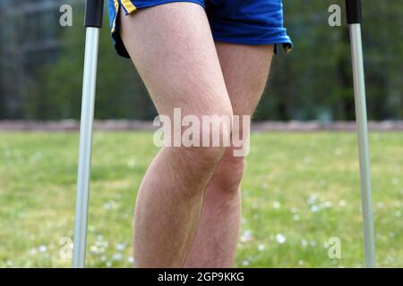 Der junge Mann in Sportbekleidung spaziert nach einem Sportunfall im Stadtpark mit Krücken Stockfoto