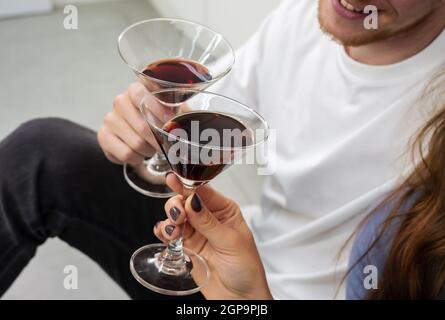 Lächelnder Mann und Frau sitzen auf dem Küchenboden und klirrende Gläser mit Cocktails. Paar Liebhaber verbringen Zeit zusammen, Spaß haben und genießen Sie ein Stockfoto