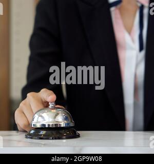 Nahaufnahme einer Geschäftsfrau, die an der Rezeption silberne Klingel klingelt. Stockfoto