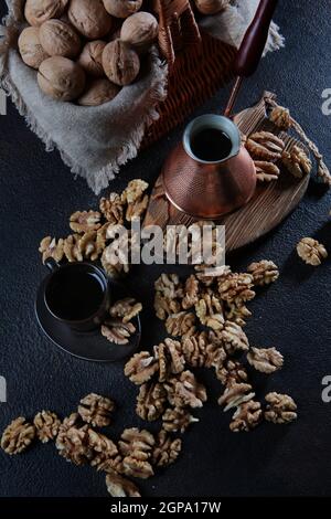 Geschälte Walnüsse auf dunklem Grund. Kaffee in einem kupfertürken. Der Kern einer Walnuss. Holzbrett. Ein Naturprodukt. Vertikales Foto. Draufsicht. Stockfoto