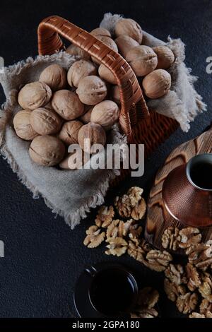 Walnüsse in einem Korb auf dunklem Grund. Kaffee in einem kupfertürken. Der Kern einer Walnuss. Holzbrett. Ein Naturprodukt. Vertikales Foto. Draufsicht. Stockfoto