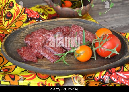 Salami-Würste in Scheiben geschnitten auf rustikalem Holzteller mit Tomaten und Rosmarin Stockfoto