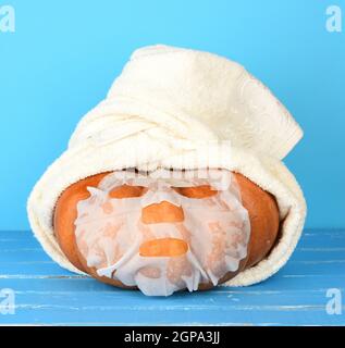 Runder orangefarbener Kürbis in ein weißes Frotteehandel, Gesichtsmaske auf der Oberfläche. Entspannungskonzept, Spa- und Schönheitsbehandlungen Stockfoto