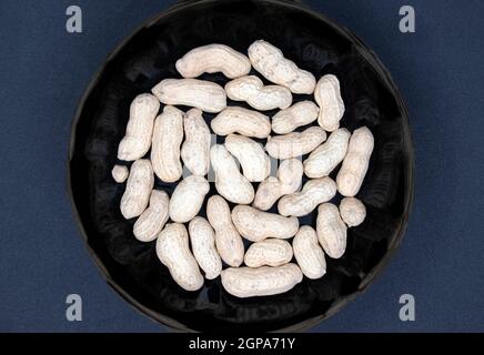 Samen von roten Erdnüssen in einer schwarzen Platte Nahaufnahme auf schwarzem Hintergrund. Stockfoto