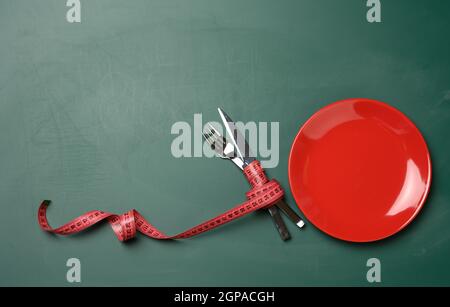 Leere rote runde Platte und Gabel und Messer in grünes Maßband auf grünem Hintergrund eingewickelt, Gewichtsverlust Konzept, flach legen Stockfoto