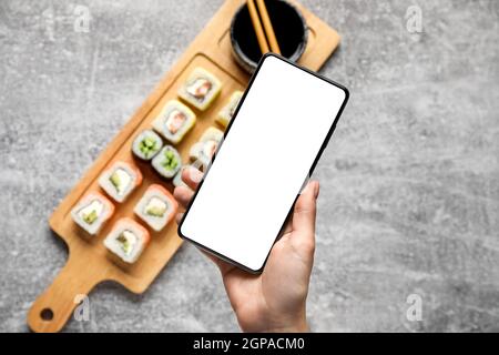 Frau mit Mobiltelefon auf grauem Hintergrund und Sushirollen, Nahaufnahme Stockfoto