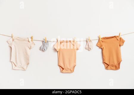 Verschiedene Babykleidung und Socken hängen an einem Seil vor weißem Hintergrund Stockfoto