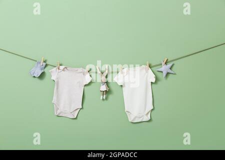 Stylische Babybodysuits, Socken und Spielzeug, die vor farbigem Hintergrund am Seil hängen Stockfoto